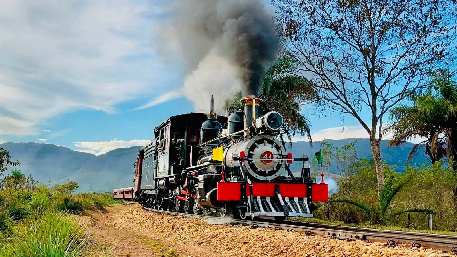 Maria-Fumaça em movimento, com a locomotiva a vapor à frente das montanhas de Minas Gerais